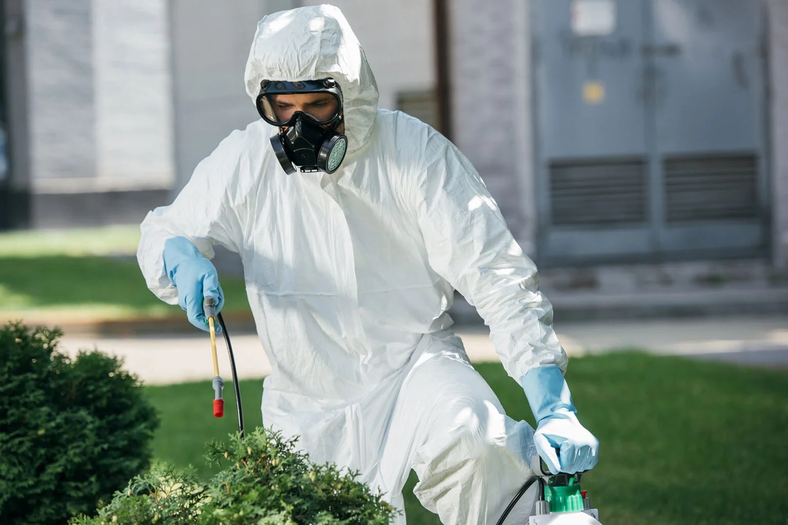Pest control technician in protective gear applying treatment outdoors